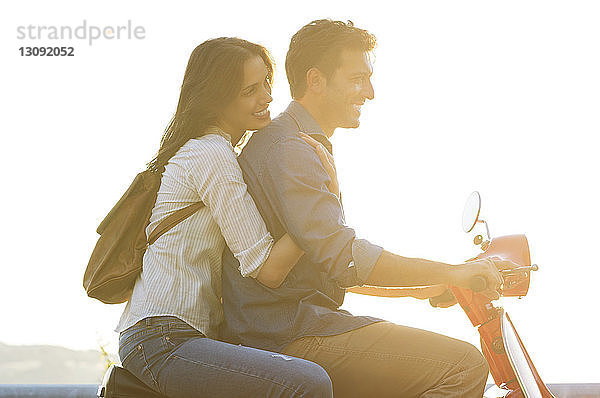 Seitenansicht eines auf einem Motorroller fahrenden Paares vor klarem Himmel an einem sonnigen Tag