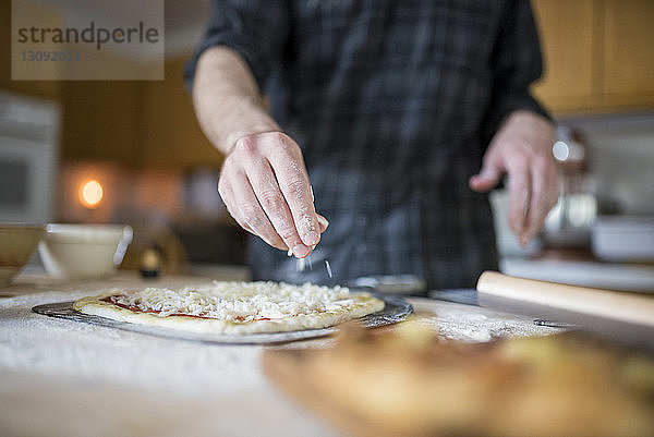 Mittelteil eines Mannes  der in der Küche Zutaten auf Pizza streut