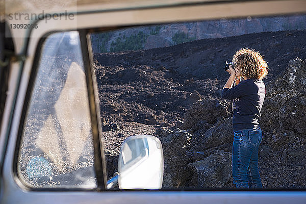 Seitenansicht einer Frau  die mit der Kamera durch das Fenster eines Wohnwagens fotografiert