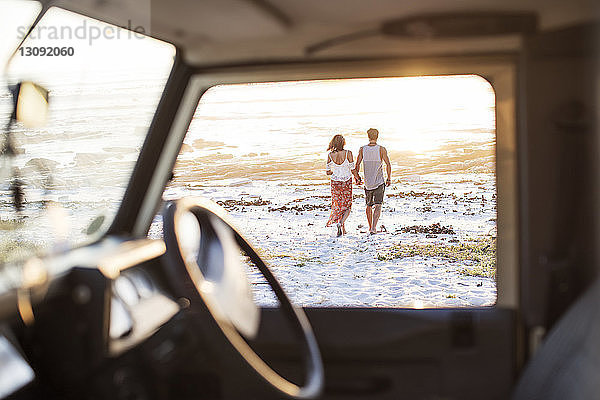 Rückansicht eines am Strand spazieren gehenden Paares durch das Fenster eines Geländewagens gesehen