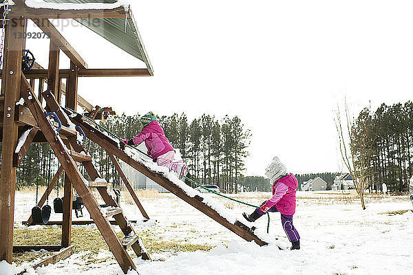 Schwestern spielen im Winter auf der Rutsche gegen den klaren Himmel