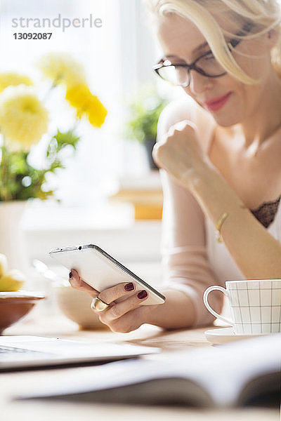 Zuversichtliche Frau benutzt Mobiltelefon  während sie zu Hause sitzt