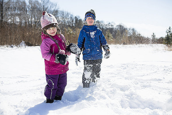 Verspielte Geschwister geniessen auf schneebedecktem Feld gegen den Himmel