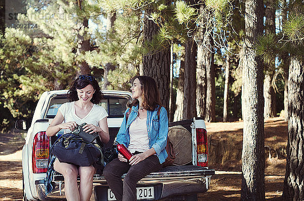 Glückliche Freundinnen unterhalten sich  während sie auf einem Pickup im Wald sitzen
