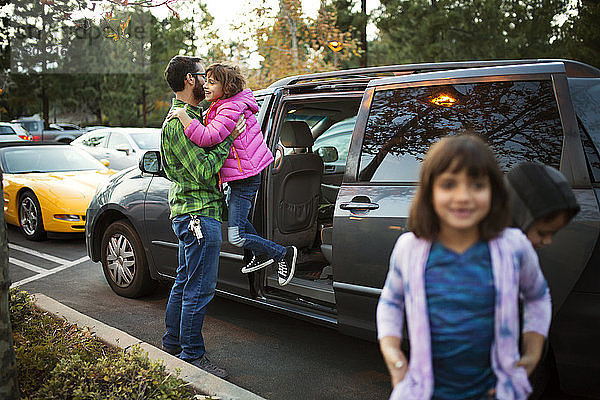 Mann hilft Tochter beim Aussteigen aus dem Auto mit Kindern im Vordergrund
