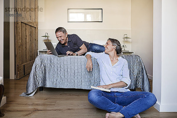 Glückliche Frau sieht älteren Mann an  der seinen Laptop im Schlafzimmer benutzt