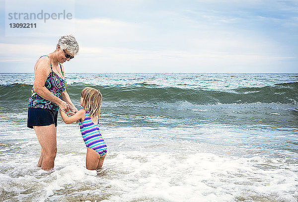 Verspielte Großmutter mit im Wasser stehender Enkelin am Strand