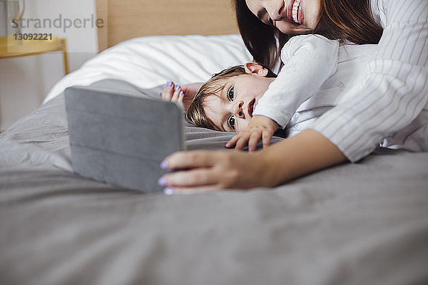 Kleinkind benutzt Tablet-Computer mit der Mutter  während es im Bett liegt