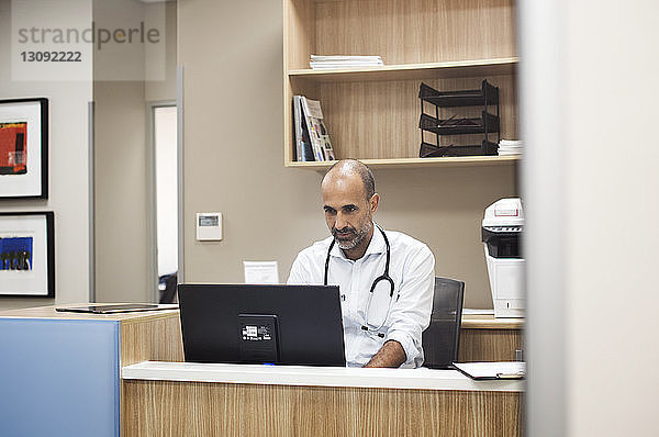 Arzt mit Desktop-Computer bei der Arbeit im Krankenhauszimmer durch Glas gesehen