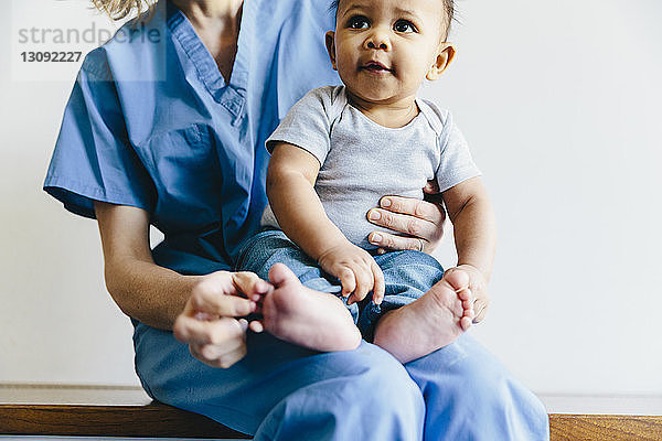 Mittelteil einer Ärztin  die einen süßen kleinen Jungen hält  während sie auf einer Bank vor weißem Hintergrund sitzt