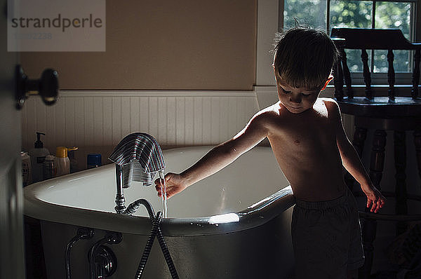 Junge ohne Hemd  der zu Hause mit Wasser in der Badewanne spielt