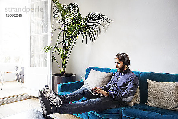 Geschäftsmann hört Musik  während er mit seinem Laptop auf dem Sofa im Büro sitzt