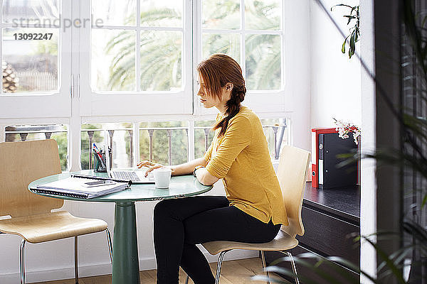 Geschäftsfrau  die auf einem Stuhl sitzt  während sie im Kreativbüro am Laptop arbeitet