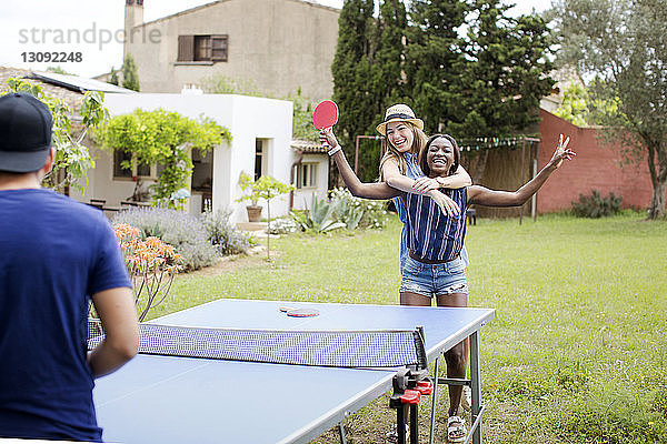 Fröhliche Frauen spielen Tischtennis mit einem Freund auf dem Hof