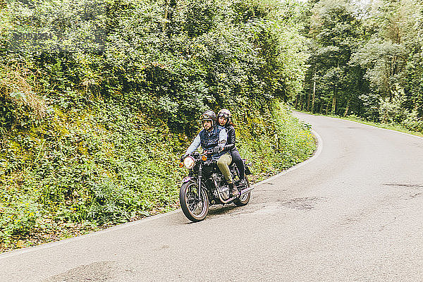 Motorradfahrendes Paar auf der Straße bei Bäumen und Pflanzen im Wald