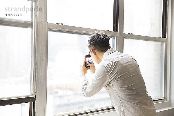 Geschäftsmann fotografiert vom Fenster aus durch ein Smartphone im Kreativbüro
