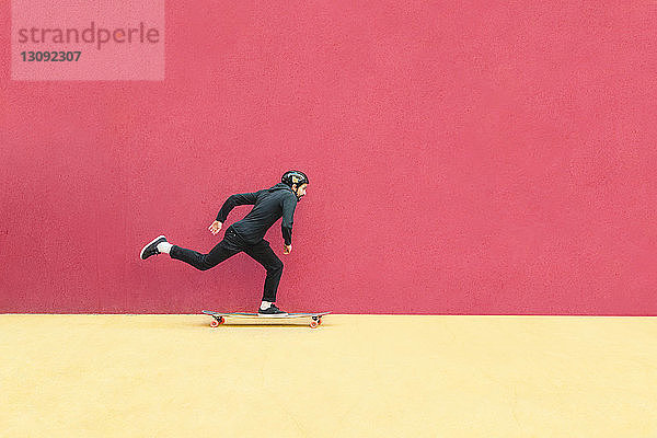 Mann fährt in voller Länge mit dem Skateboard gegen die Wand