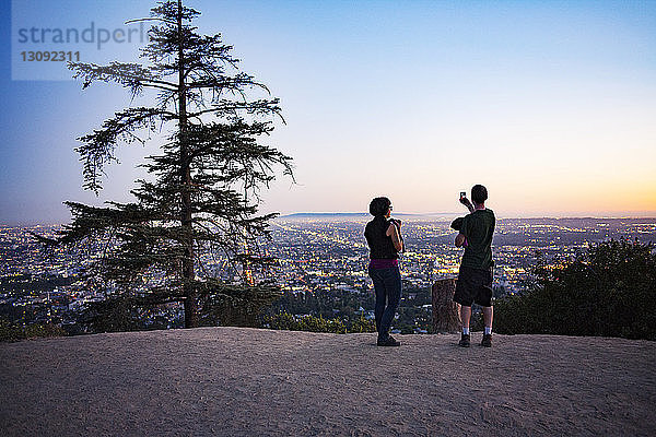 Silhouette von zwei Personen  die in der Abenddämmerung im Griffith Park Fotos vom Stadtbild machen