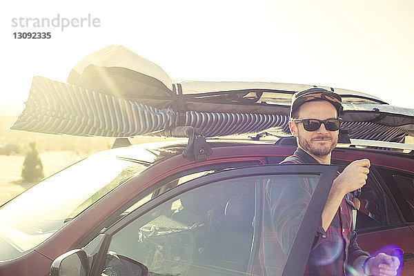 Lächelnder Mann steigt an einem sonnigen Tag vor klarem Himmel aus einem beladenen Auto