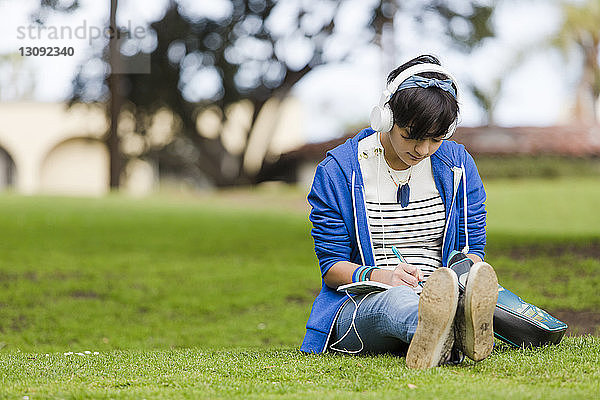 Teenager-Mädchen schreibt in voller Länge auf Tagebuch  während sie im Park Musik hört