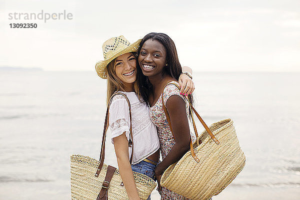 Porträt von glücklichen Freundinnen in Seitenansicht  die sich umarmen  während sie am Strand am Ufer stehen