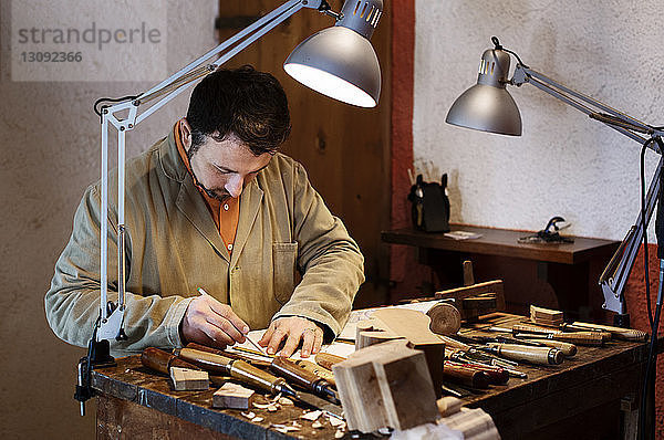 Handwerker  der in einer Werkstatt einen Entwurf für eine Figur auf einem Tisch entwirft
