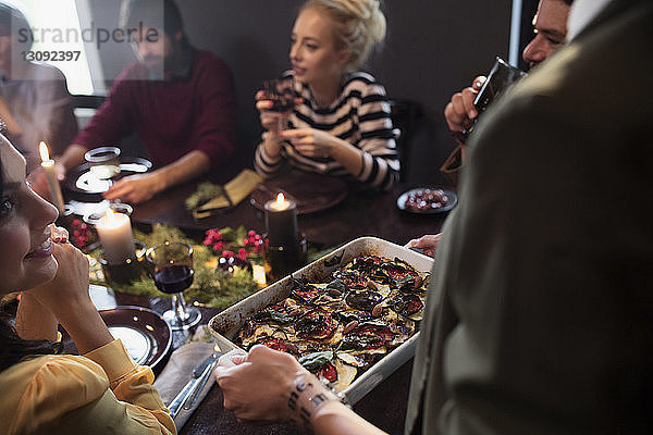 Frau serviert glücklichen Freunden am Tisch während der Weihnachtsfeier Essen