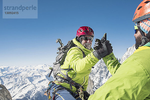 Wanderer unterstützt Freund beim Bergsteigen gegen den klaren blauen Himmel im Winter