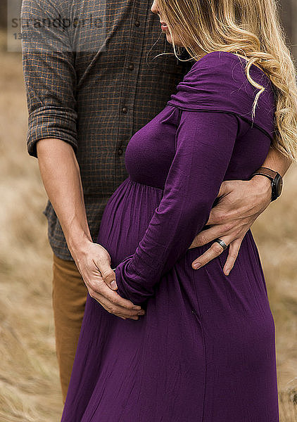 Mittelteil des Ehemannes  der die schwangere Frau umarmt  während er im Freien steht