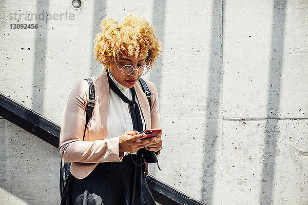 Frau benutzt Smartphone  während sie an der Wand steht