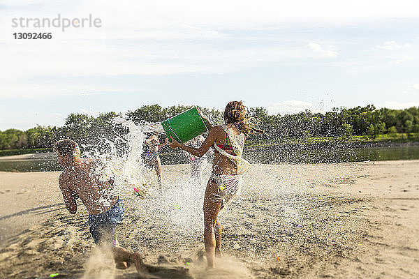 Freunde spielen mit Wasser am Strand gegen den Himmel