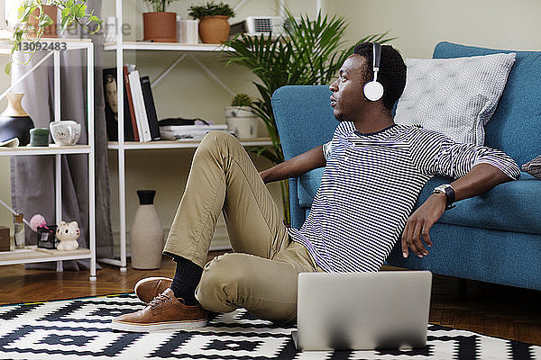 Nachdenklicher Mann hört Musik  während er im Wohnzimmer auf dem Boden sitzt
