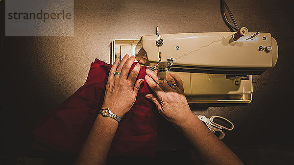Hochwinklig abgeschnittene Hände einer Frau  die in der Werkstatt eine Nähmaschine benutzt