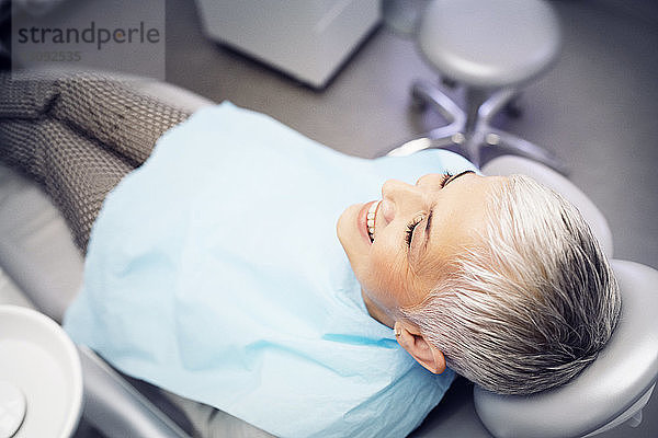 Hochwinkelansicht einer lächelnden Frau  die auf einem Zahnarztstuhl sitzt