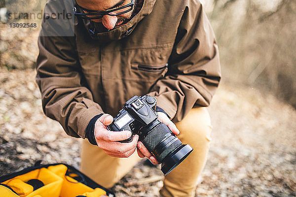 Männlicher Wanderer stellt Kamera ein  während er auf einem Feld im Wald kniet