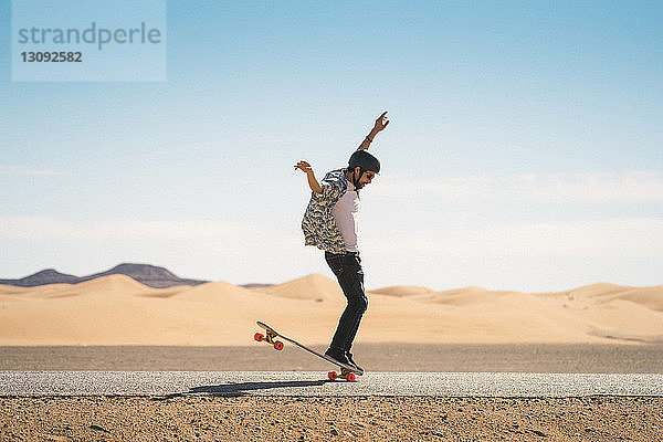 Mann fährt Skateboard auf der Straße gegen blauen Himmel bei Sonnenschein