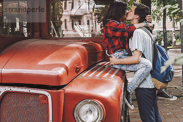 Seitenansicht eines jungen Paares  das sich in der Stadt mit einem Oldtimer-Bus auf den Mund küsst