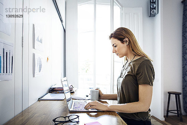 Seitenansicht einer Geschäftsfrau mit Laptop  die am Schreibtisch im Kreativbüro sitzt