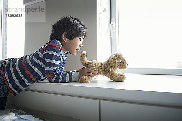 Junge spielt zu Hause mit Stofftier auf Fensterbank