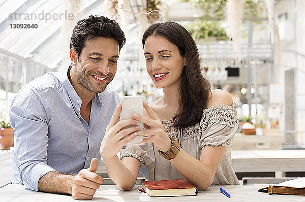 Glückliches Paar benutzt Smartphone im Straßencafé