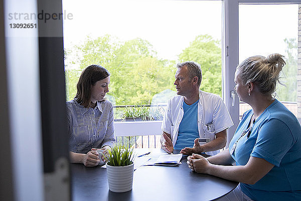 Ärzte sprechen mit Patientin  während sie in einer medizinischen Klinik am Tisch sitzen