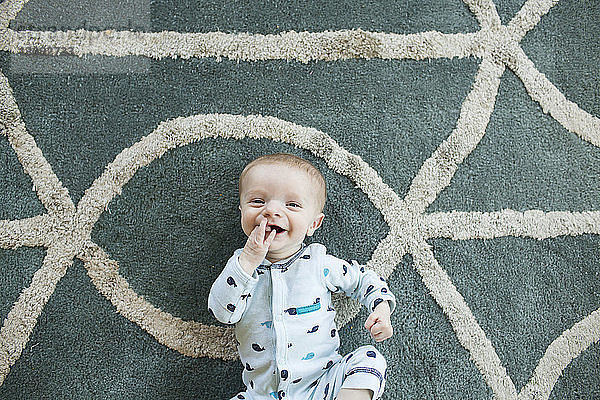 Portrait eines fröhlichen kleinen Jungen  der zu Hause auf einem Teppich liegt