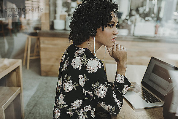 Frau hört Musik  während sie mit Laptop-Computer am Tisch im Café sitzt