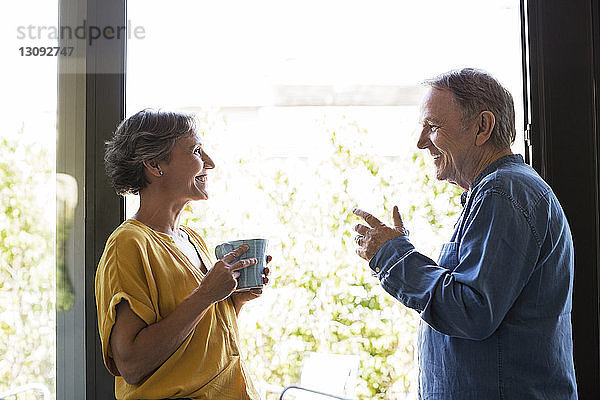 Seitenansicht eines älteren Ehepaares beim Kaffee trinken am Fenster zu Hause