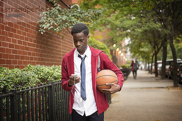 Schüler telefoniert und hält Basketball beim Gehen auf dem Bürgersteig