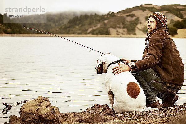 Reisende beim Angeln mit Hund am Seeufer sitzend