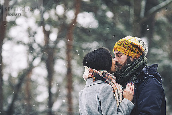 Romantisches Paar küsst sich im Winter stehend im Wald