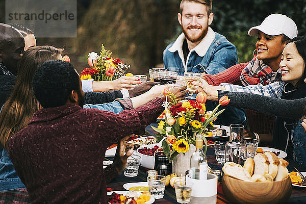 Freunde stoßen Wein an  während sie im Hinterhof am Tisch sitzen