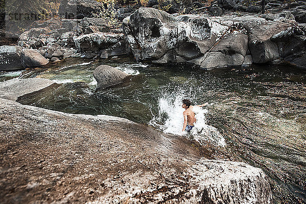 Wanderer genießt im Fluss gegen Felsen im Wald