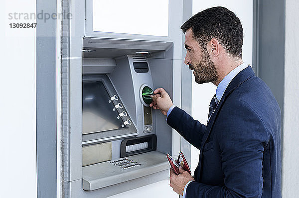 Seitenansicht eines Geschäftsmannes  der an der U-Bahn-Station einen Geldautomaten benutzt